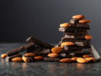 Broken dark chocolate bar with almond on a black background. Copy space.